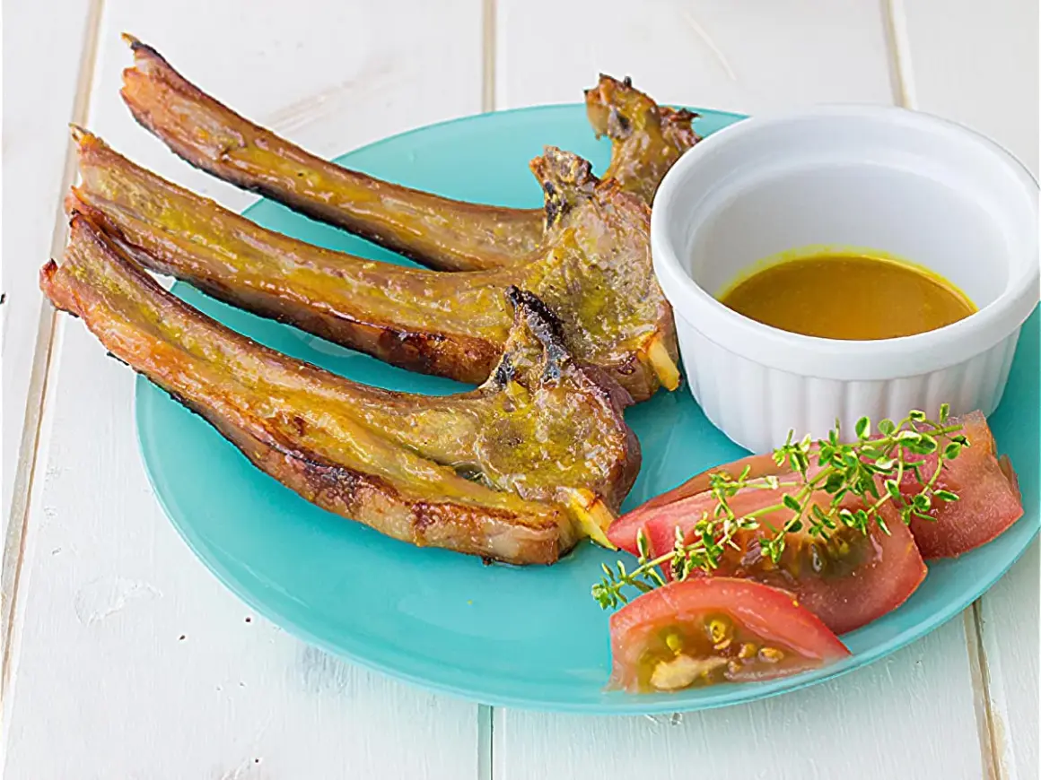 Chuletas de cordero al horno, doradas y jugosas, servidas con una salsa dorada, rodajas de tomate y ramitas de tomillo fresco.