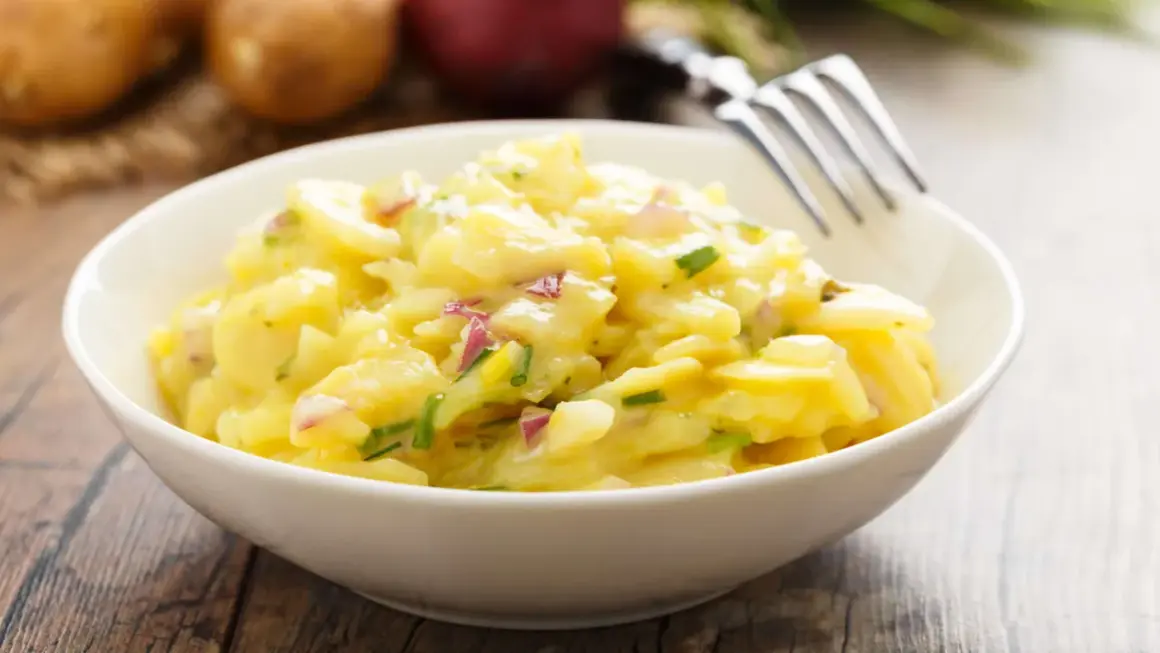 Schüssel mit cremigem Kartoffelsalat, garniert mit Schnittlauch und roten Zwiebeln. Perfekt für 7 Tassen Salat.