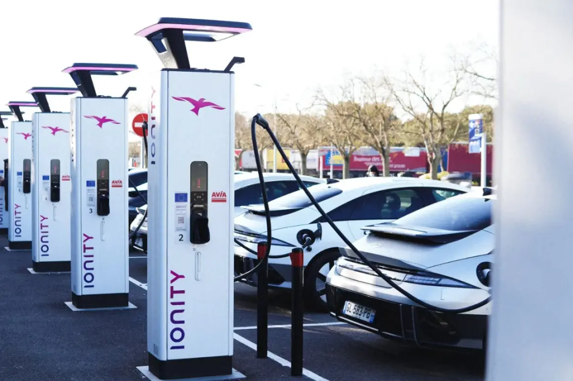 Une rangée de bornes de recharge IONITY attend des véhicules électriques. Des voitures modernes sont garées, prêtes à être chargées.