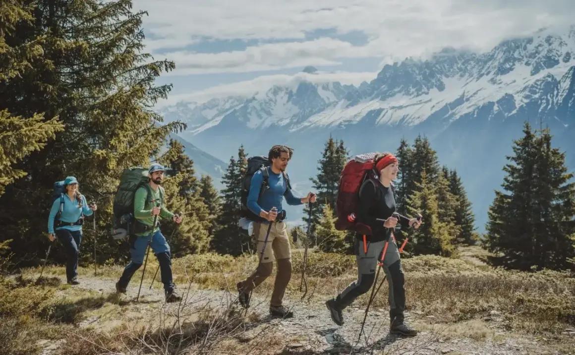Cuatro personas con mochilas grandes caminan por un sendero montañoso. La diferencia entre senderismo y montañismo se ve en su equipo y el terreno.