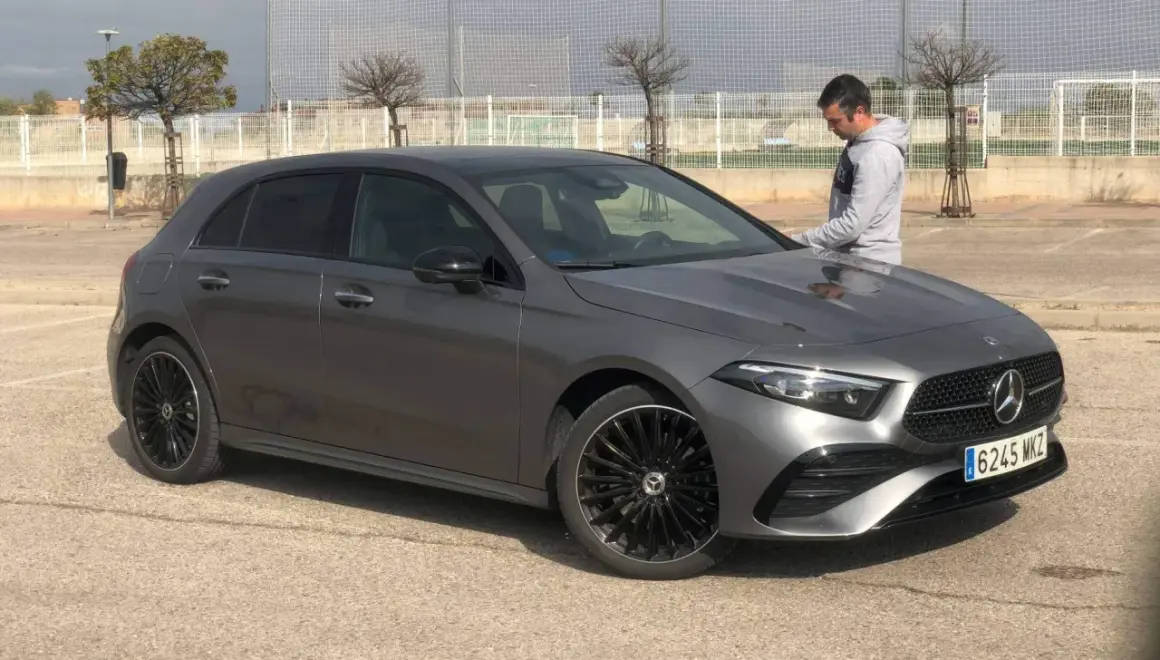 Un hombre se apoya en un elegante Mercedes Clase A gris oscuro, listo para un viaje.