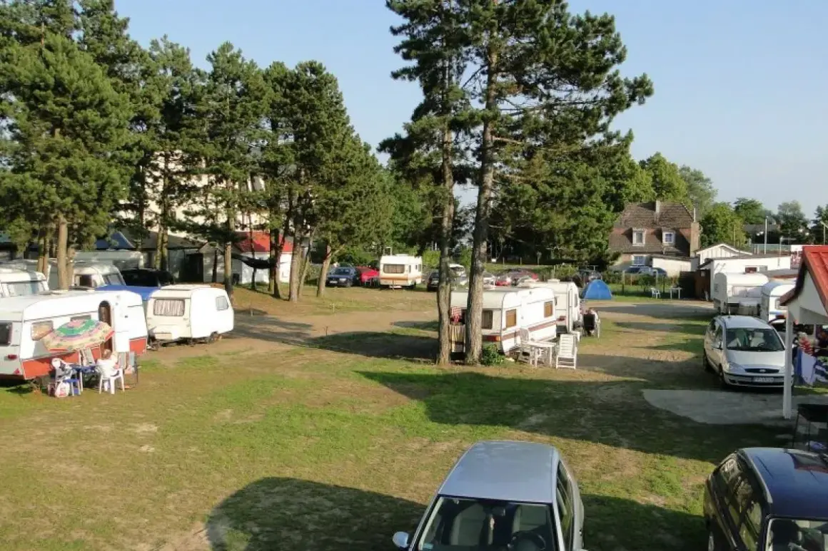Wypoczynek na kempingu nad Bałtykiem w Mielnie. Przyczepy kempingowe i samochody na trawiastym terenie, otoczone drzewami.