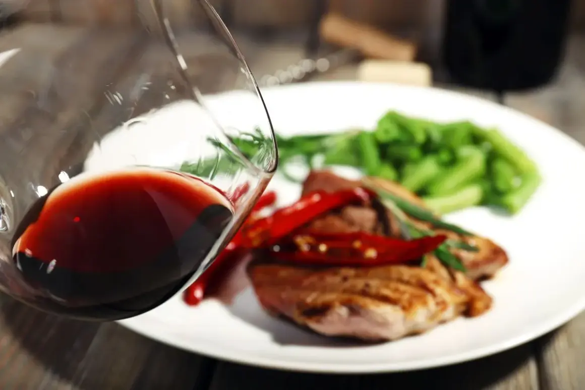Czerwone wino w kieliszku, idealne do wieprzowiny z papryczkami chili i zieloną fasolką. Pyszny obiad czeka!