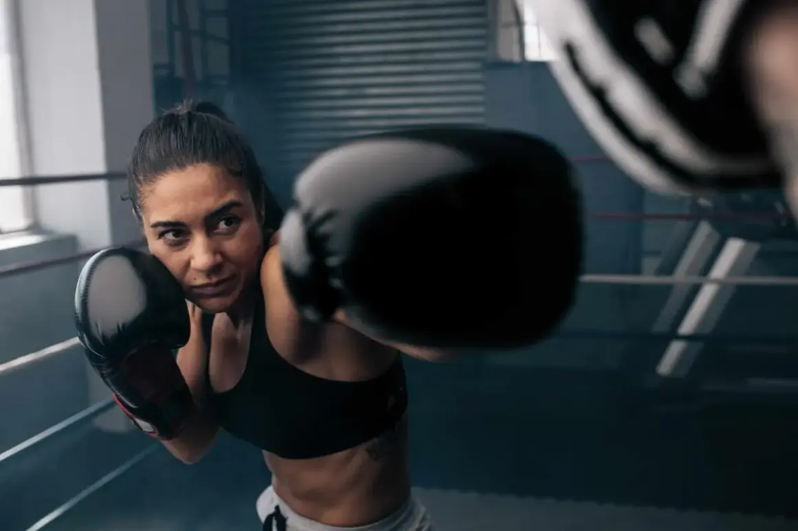 Woman in boxing gloves throws a punch during an intense boxing workout online.
