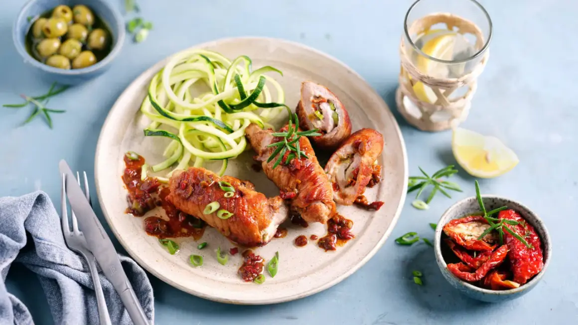 Herzhafte involtini vom Kalb mit Zucchini-Spaghetti und einer würzigen Tomatensauce, garniert mit Rosmarin.