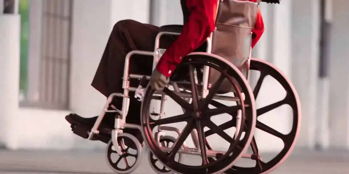Osoba na wózku inwalidzkim w czerwonej koszuli i czarnych spodniach porusza się po chodniku.