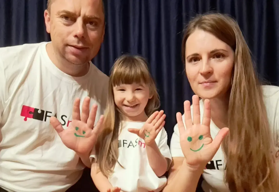 Rodzina w koszulkach z logo FAS. Na dłoniach narysowane uśmiechnięte buźki. Co to FAS? To pytanie, na które warto znać odpowiedź.