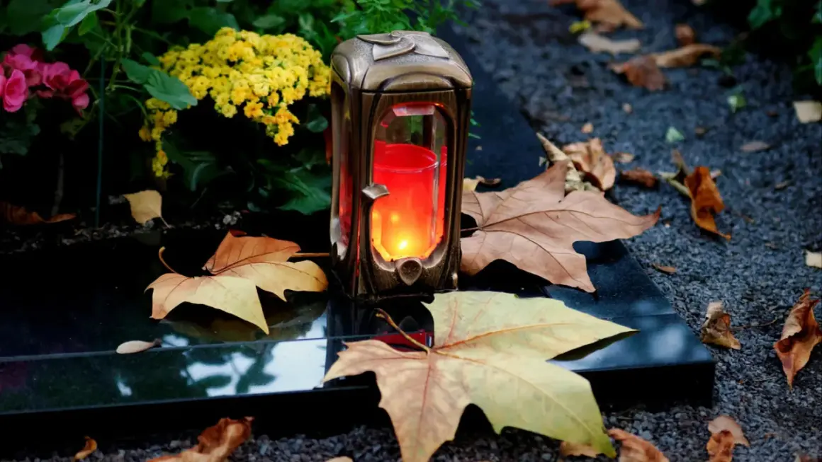 Grablicht auf einem Grabstein, umgeben von Herbstlaub und Blumen. Ein stiller Gruß zu Allerheiligen katholisch.