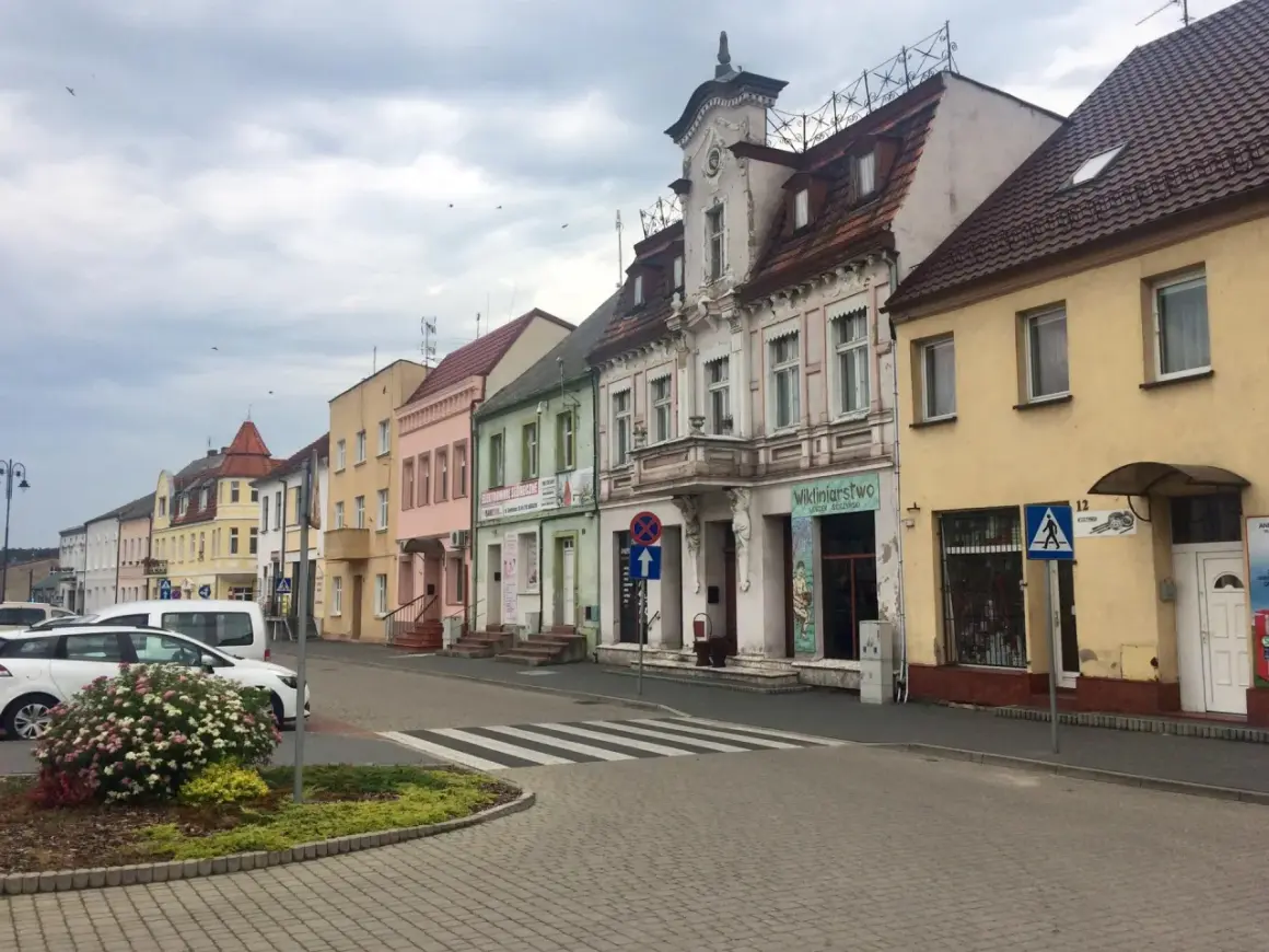 Kolorowe kamienice w **Złotnikach Kujawskich** przy ulicy, z samochodami i zielenią.