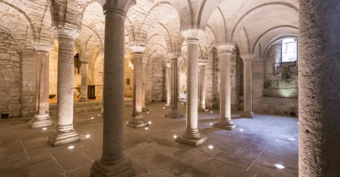 Cripta dell'Abbazia di San Salvatore, con colonne in pietra e volte a crociera illuminate da faretti a pavimento.