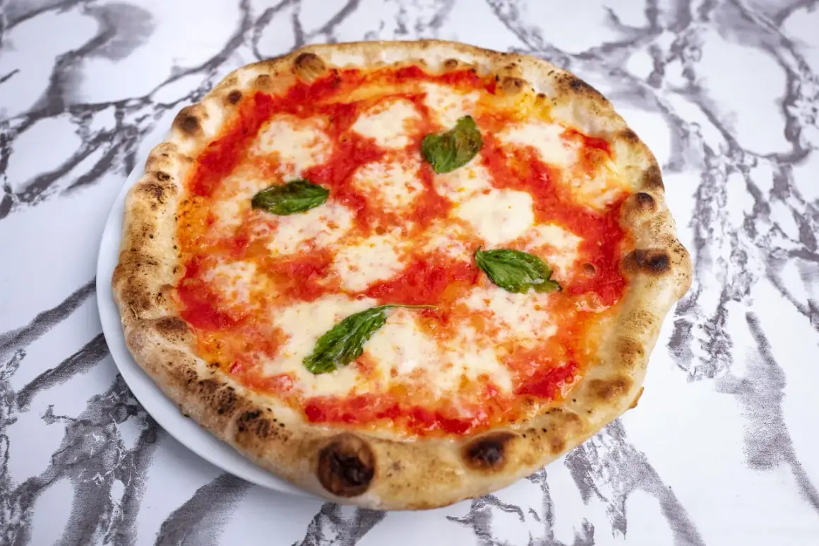 Pyszna pizza napoletana z pomidorami, mozzarellą i bazylią, z lekko przypieczonym brzegiem, na marmurowym tle.