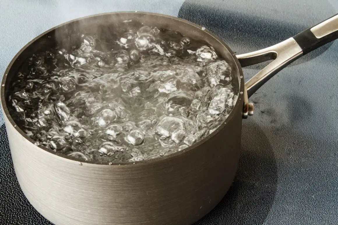Une casserole en métal sur une plaque de cuisson, l'eau est en train de bouillir avec des bulles et de la vapeur.