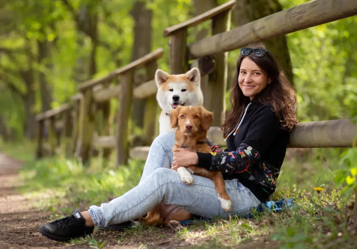 Kobieta z dwoma psami w lesie. Jeden piesek jest na jej kolanach, drugi za nim. Wskazówki, jak uspokoić sukę podczas cieczki, mogą być pomocne.