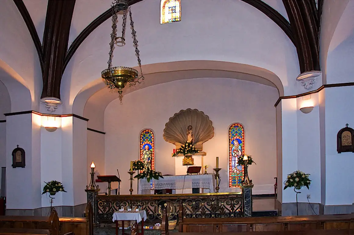 Interior de la iglesia de conchas Galicia, con altar, vitrales y lámpara colgante.