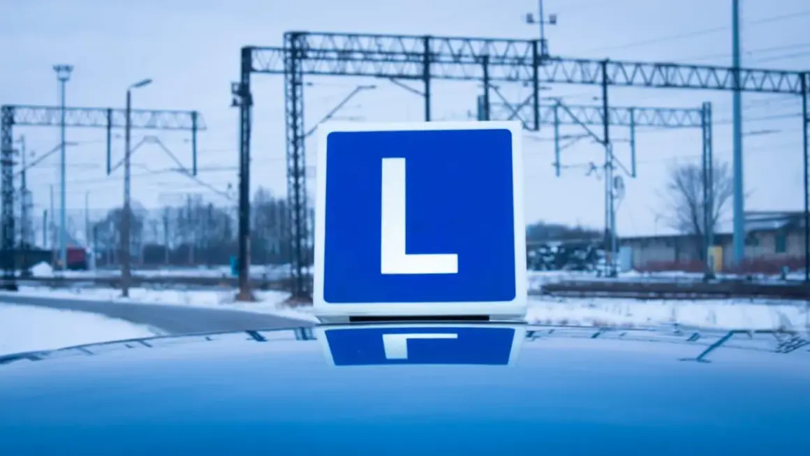 Niebieska tablica z literą "L" na dachu samochodu, symbolizująca naukę jazdy i przyszłe testy na kierowcę.