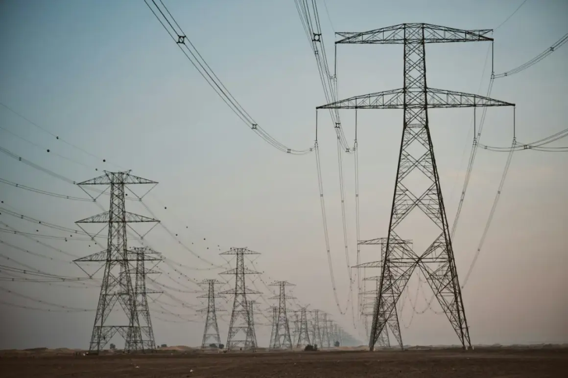 Linia wysokiego napięcia z wieżami energetycznymi, przypominającymi gigantyczne kogeneratory, ciągnie się przez pustynny krajobraz.