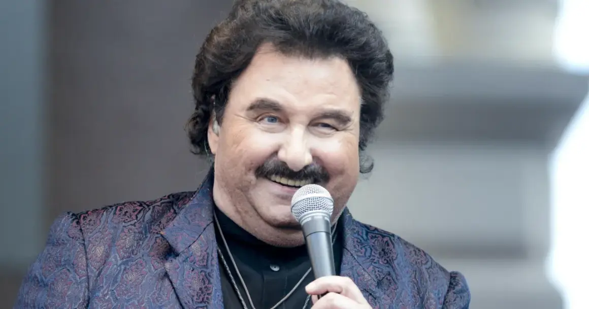 Krzysztof Krawczyk śpiewa "Byle było tak..." z mikrofonem w dłoni, w ozdobnej marynarce.