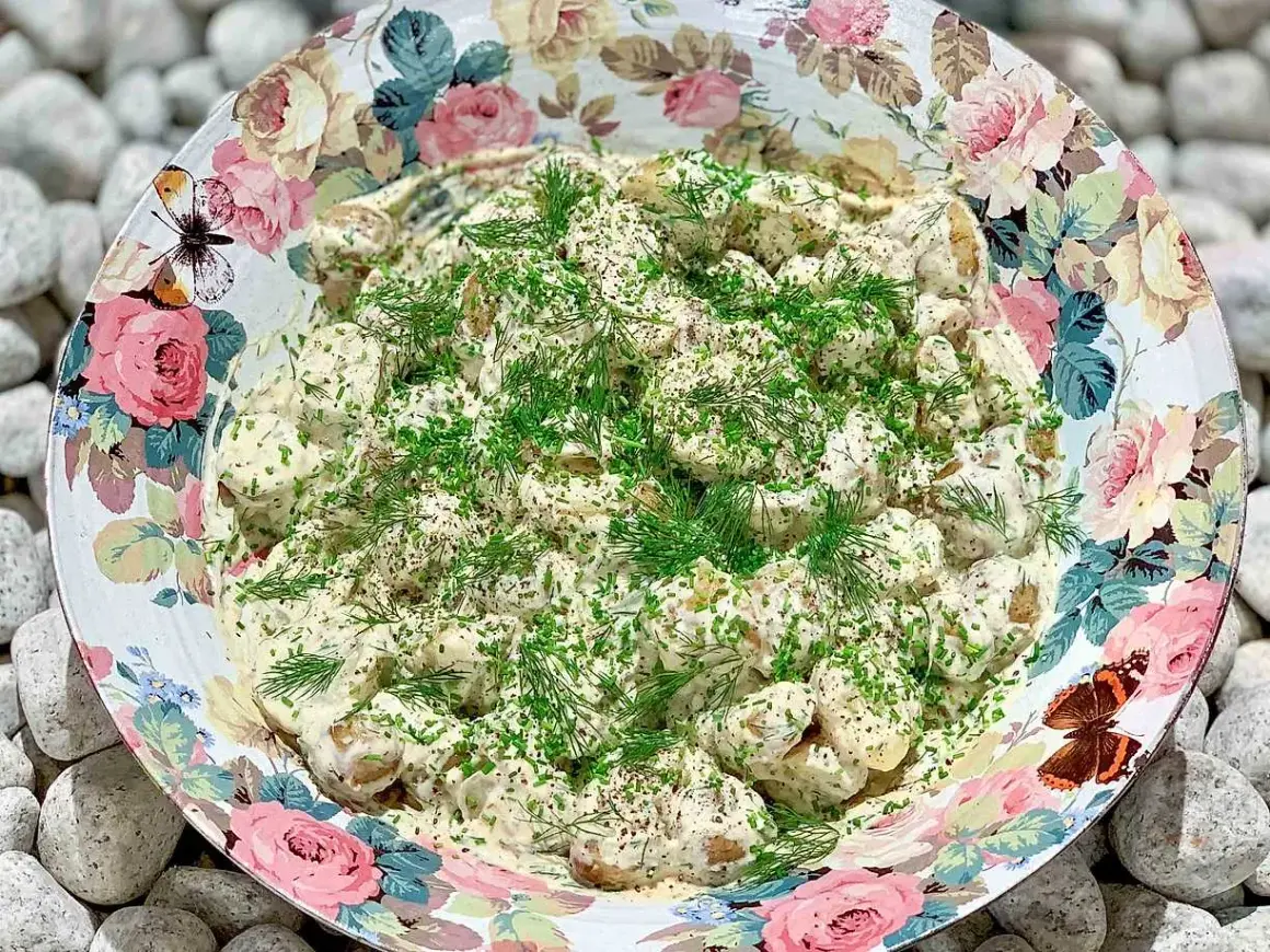 Enkel potatissallad med krämig crème fraiche, toppad med färska örter. Serveras i en vacker skål med blomstermönster.