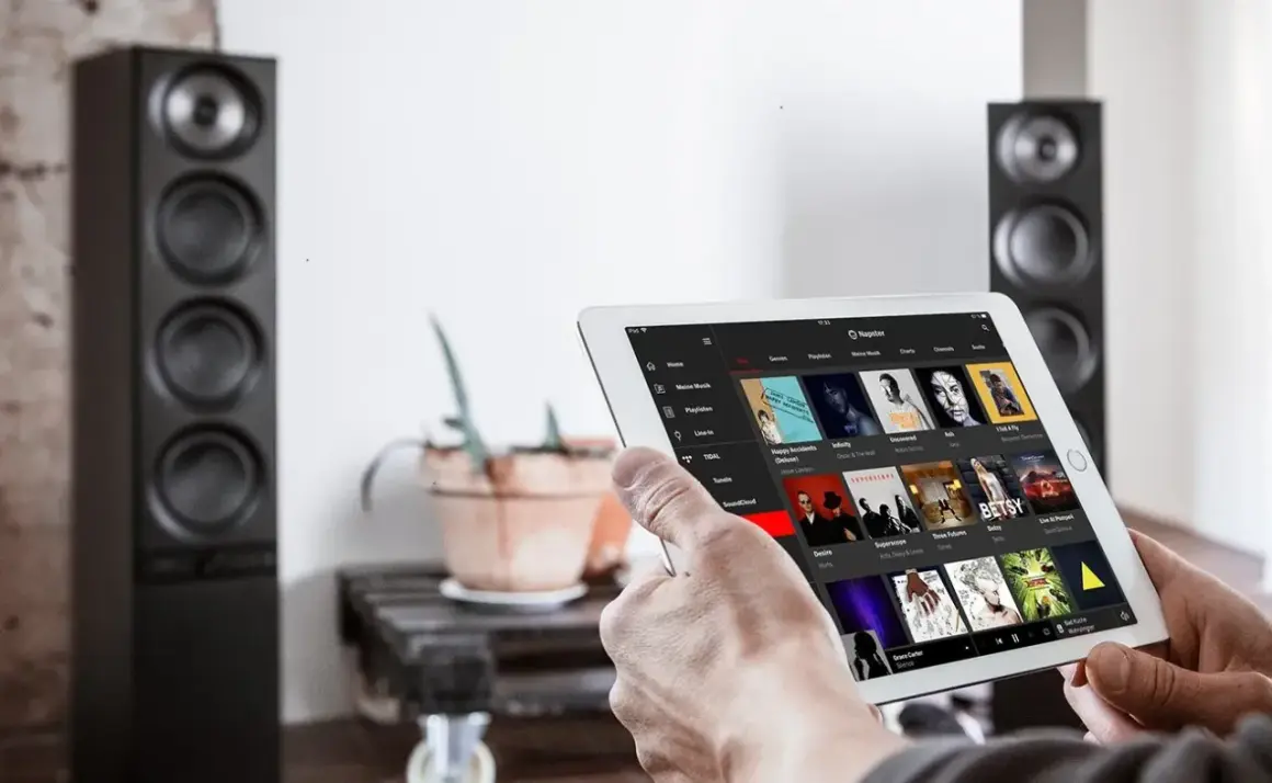 Mann sucht auf einem Tablet nach neue Musik. Im Hintergrund stehen zwei schwarze Lautsprecher.