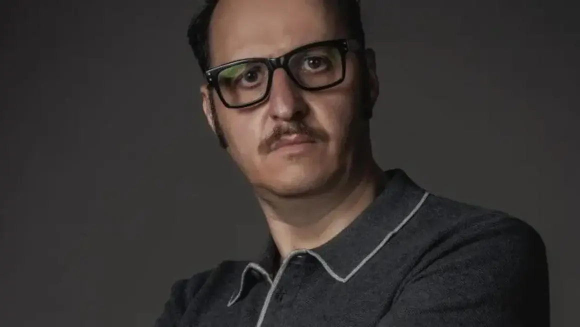 Ritratto di Fausto Russo Alesi con occhiali neri e baffi, indossa una polo grigia.