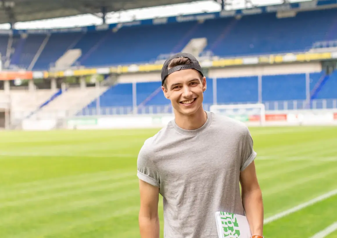 Junger Mann mit Kappe und Buch im Stadion, bereit für seinen Eventmanagement Master.