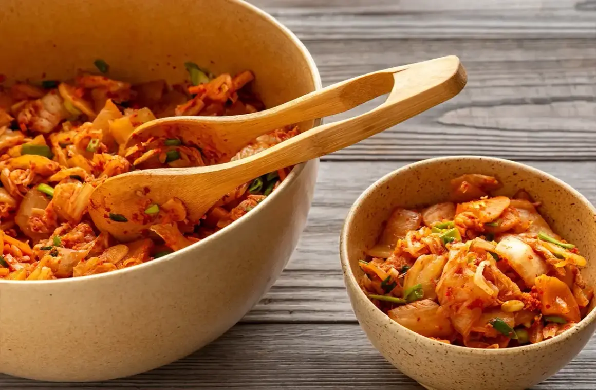 Två skålar med kryddig, fermenterad mat, troligen kimchi, med träskedar i den större skålen.