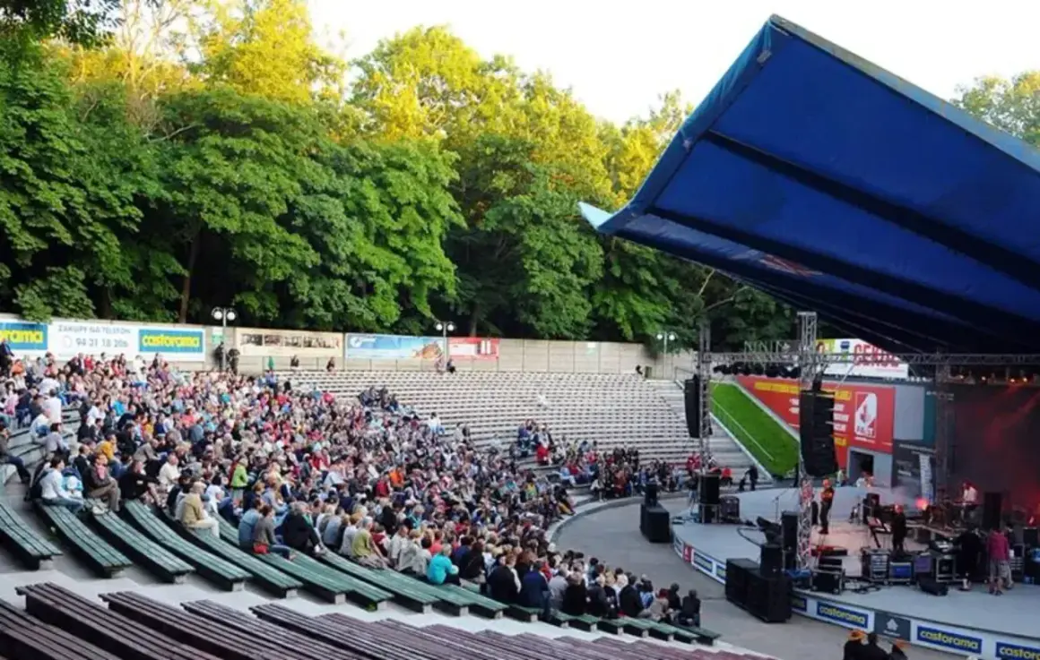 Tłum widzów na koncercie w amfiteatrze w Kołobrzegu. Scena z zespołem muzycznym i niebieski dach nad widownią.
