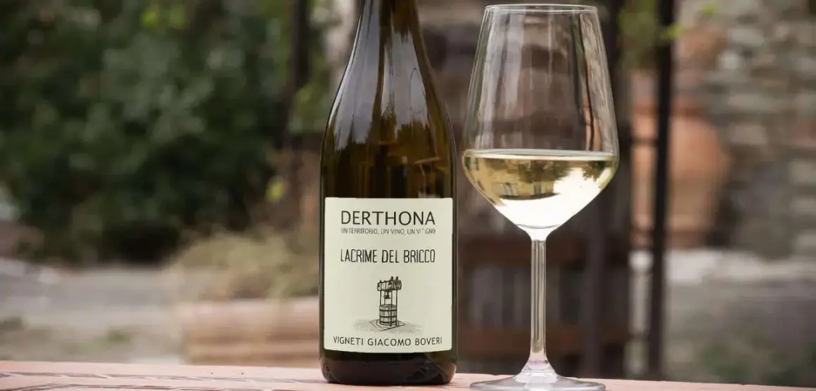 Calice e bottiglia di Derthona, vino Timorasso. Le caratteristiche di questo vino bianco piemontese sono freschezza e note minerali.