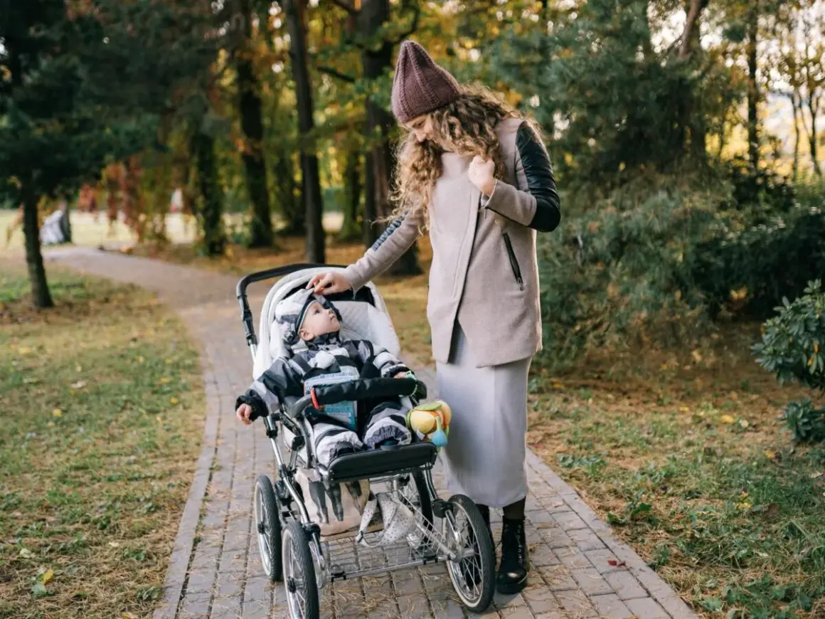Mama poprawia czapkę malucha, który siedzi w spacerówce. Jesienny spacer po parku.