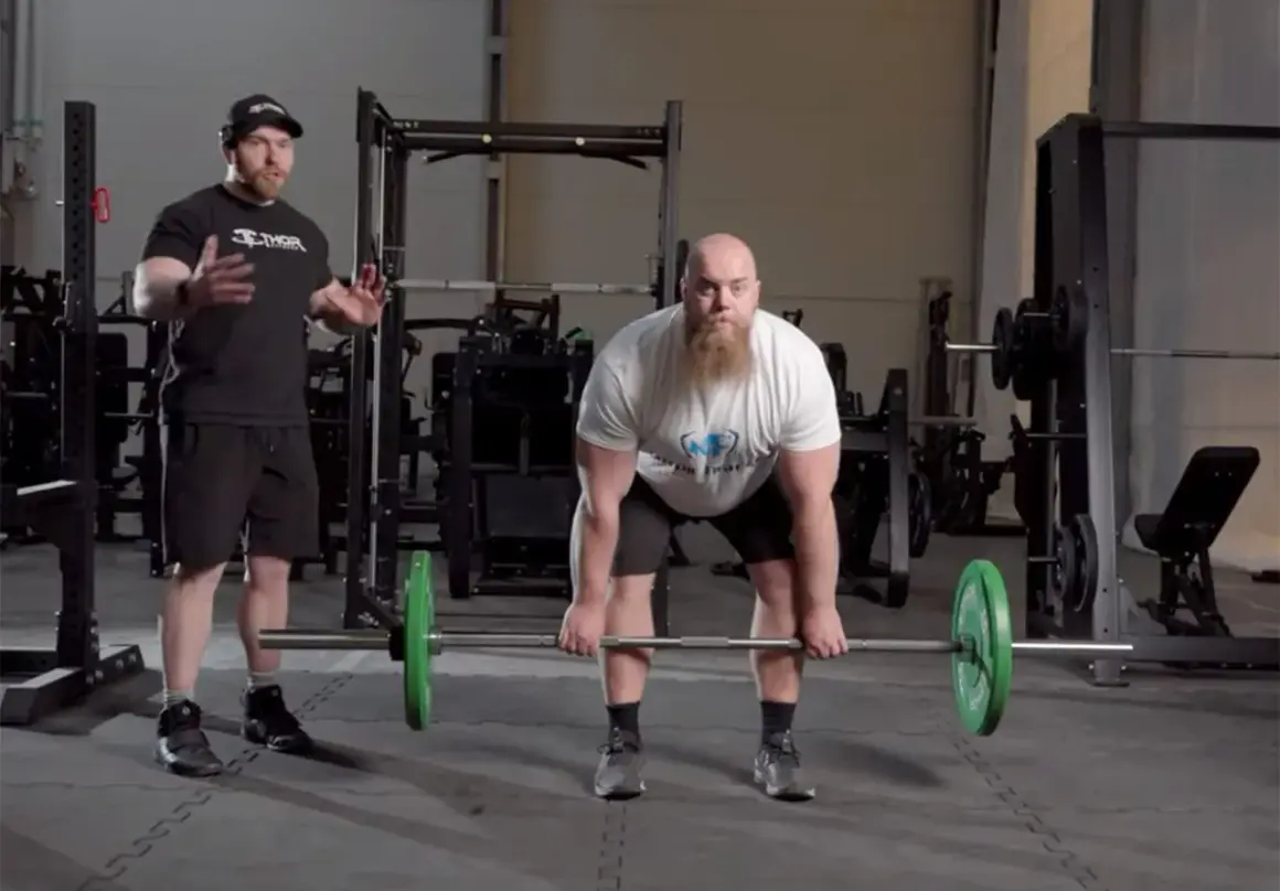 Instruktör visar rdl teknik för en man med skägg som förbereder sig för ett marklyft i ett gym.