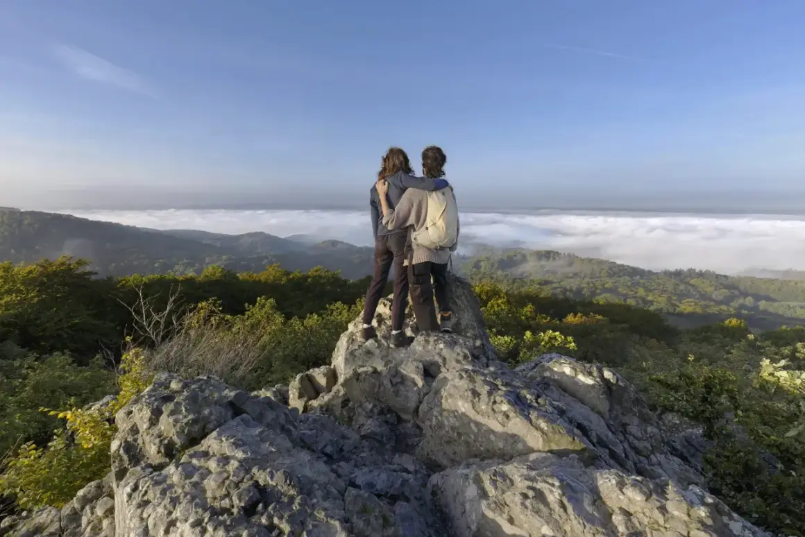 Zwei Freunde genießen den Ausblick beim Wandern an der Sieg. Nebel liegt im Tal, die Sonne scheint auf die Berge.