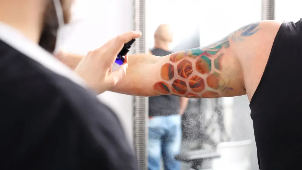 Ein frisches Tattoo mit Rosen in Wabenform wird besprüht. Der Träger ruht sich aus, während die Pflege beginnt.