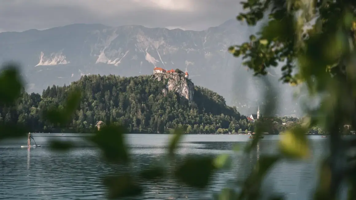 Jezioro Bled ze skalnym zamkiem, jedno z najpiękniejszych miejsc w Słowenii. Na pierwszym planie widać osobę na desce SUP.