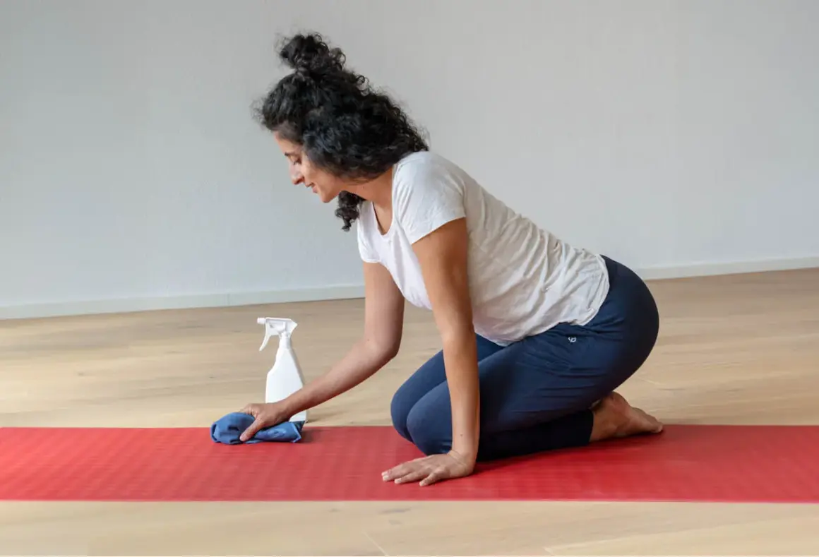 Frau reinigt ihre naturkautschuk yogamatte mit einem Tuch und Sprühflasche.