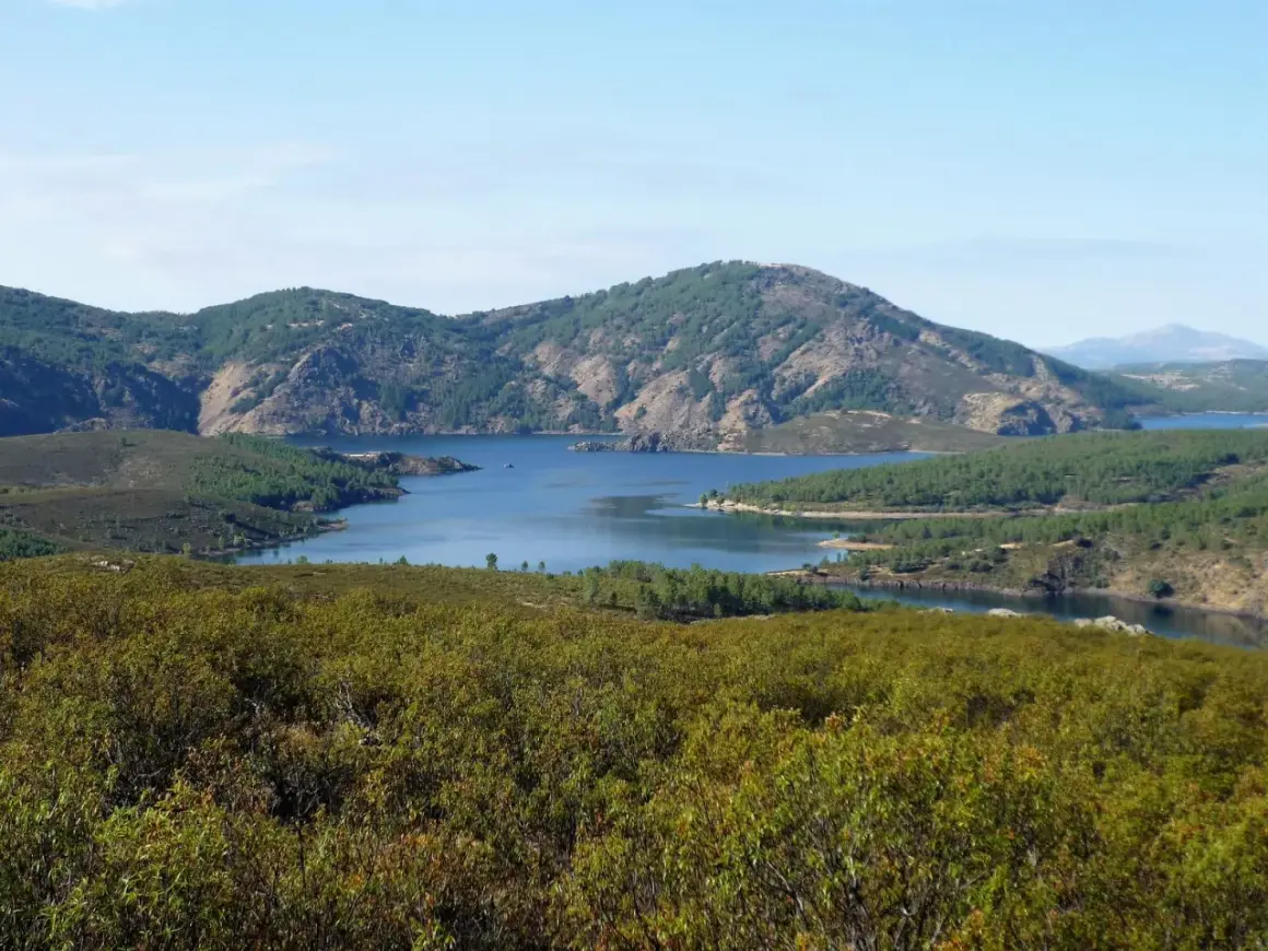 Paisaje sereno con un embalse azul rodeado de montañas verdes. La senda del Genaro se adentra en este idílico entorno natural.