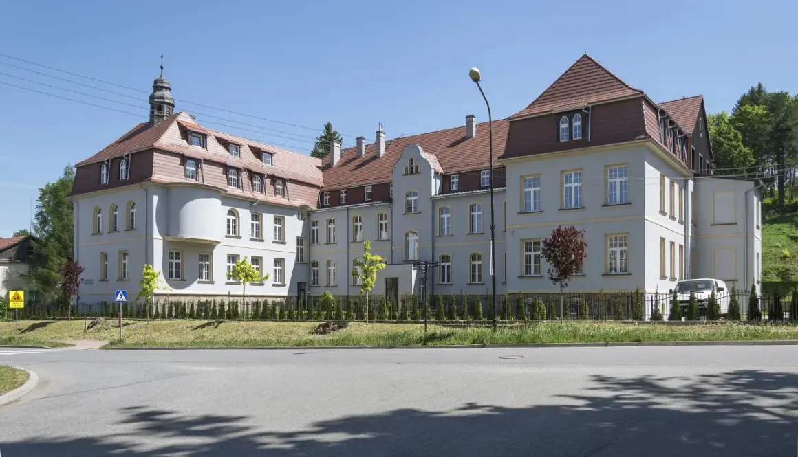 Elegancki budynek z wieżyczką, gdzie mieści się dom seniora Magda lenka, otoczony zielenią.