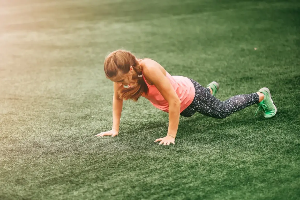 Une femme en tenue de sport fait des pompes sur une pelouse synthétique, un entraînement typique de boot camp sport.