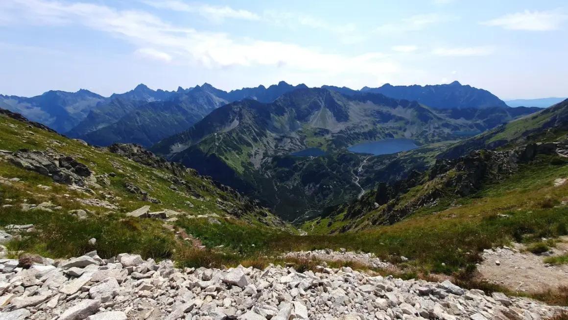Widok z przełęczy na skraju Orlej Perci na Tatry Wysokie. Dwa jeziora w dolinie, skaliste zbocza i szczyty w oddali.