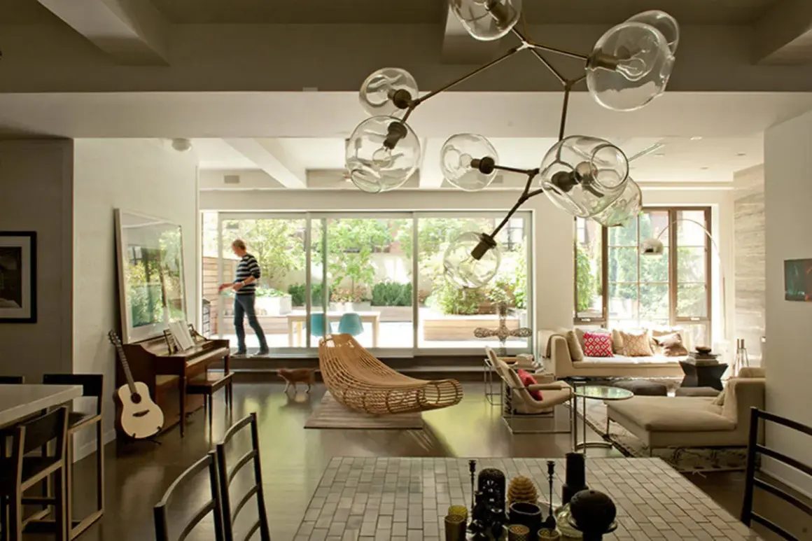 A man walks through a modern living room, captured in this interior architecture photography. A piano, guitar, and unique light fixture are visible.
