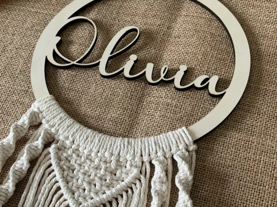 Un bel attrape-rêve personnalisé pour fabriquer un attrape rêve avec prénom. Le prénom "Olivia" est inscrit en lettres de bois sur un cercle orné de macramé.