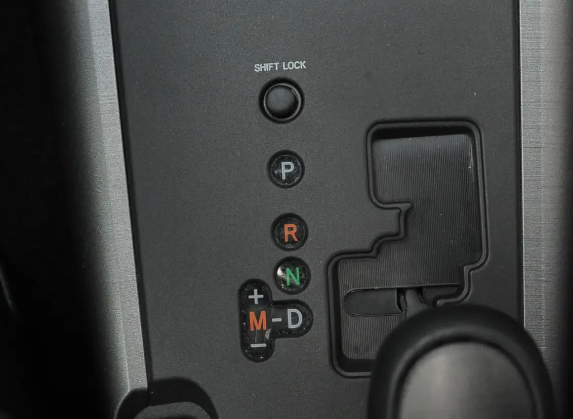 Panel z przyciskami skrzyni biegów: P, R, N, M-D. Obok przycisku "SHIFT LOCK" znajduje się otwór do jego zwolnienia.
