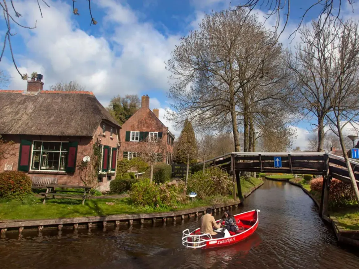 Paseo en barca por los canales de Giethoorn, Holanda, con casas de tejado de paja y un puente de madera.