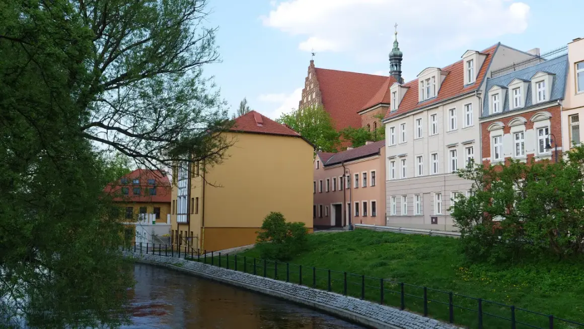 Nad rzeką malownicze kamienice. Chcesz wiedzieć, jak sprawdzić czy budynek jest w rejestrze zabytków? Spójrz na detale architektoniczne i wieżę kościelną.