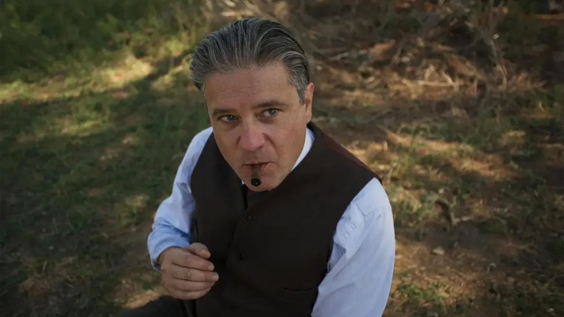 Un uomo con un sigaro in bocca, vestito elegantemente, sembra un re.