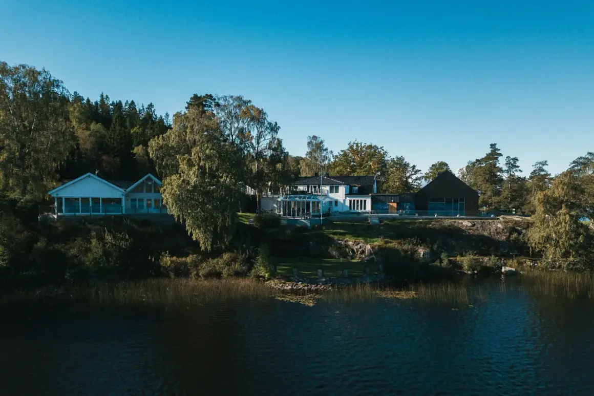 Hällsnäs Hotell & Restaurang vid en sjö, omgivet av träd. En vacker plats för avkoppling och god mat.