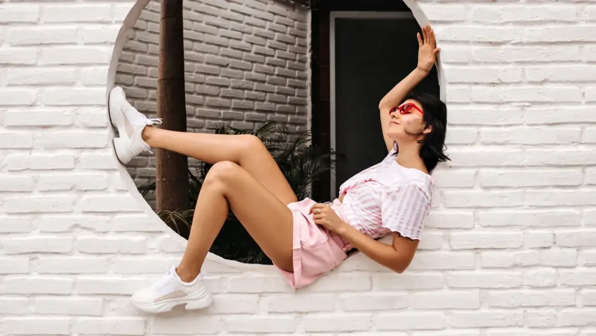 Ragazza con occhiali rossi e cljd scarpe bianche, sdraiata su un davanzale bianco.