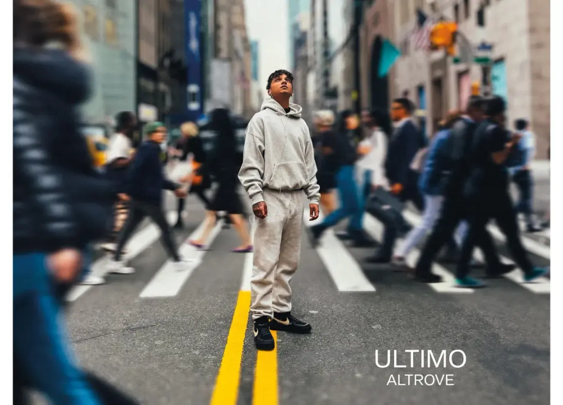 A young man in a grey tracksuit stands on a crosswalk in a busy city street, looking up.