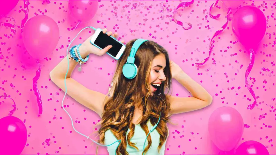 A young woman with headphones on, holding a smartphone, surrounded by pink balloons and confetti.