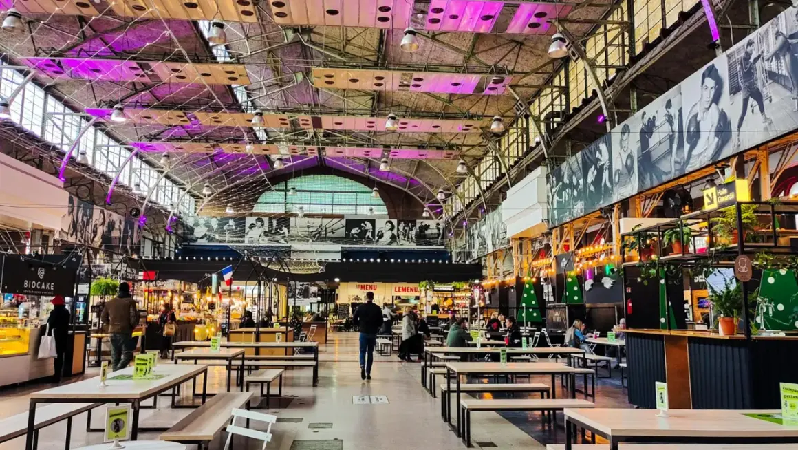 Wnętrze nowoczesnej vege restauracji w Warszawie. Widać stoły, ławki i stoiska z jedzeniem pod industrialnym dachem.