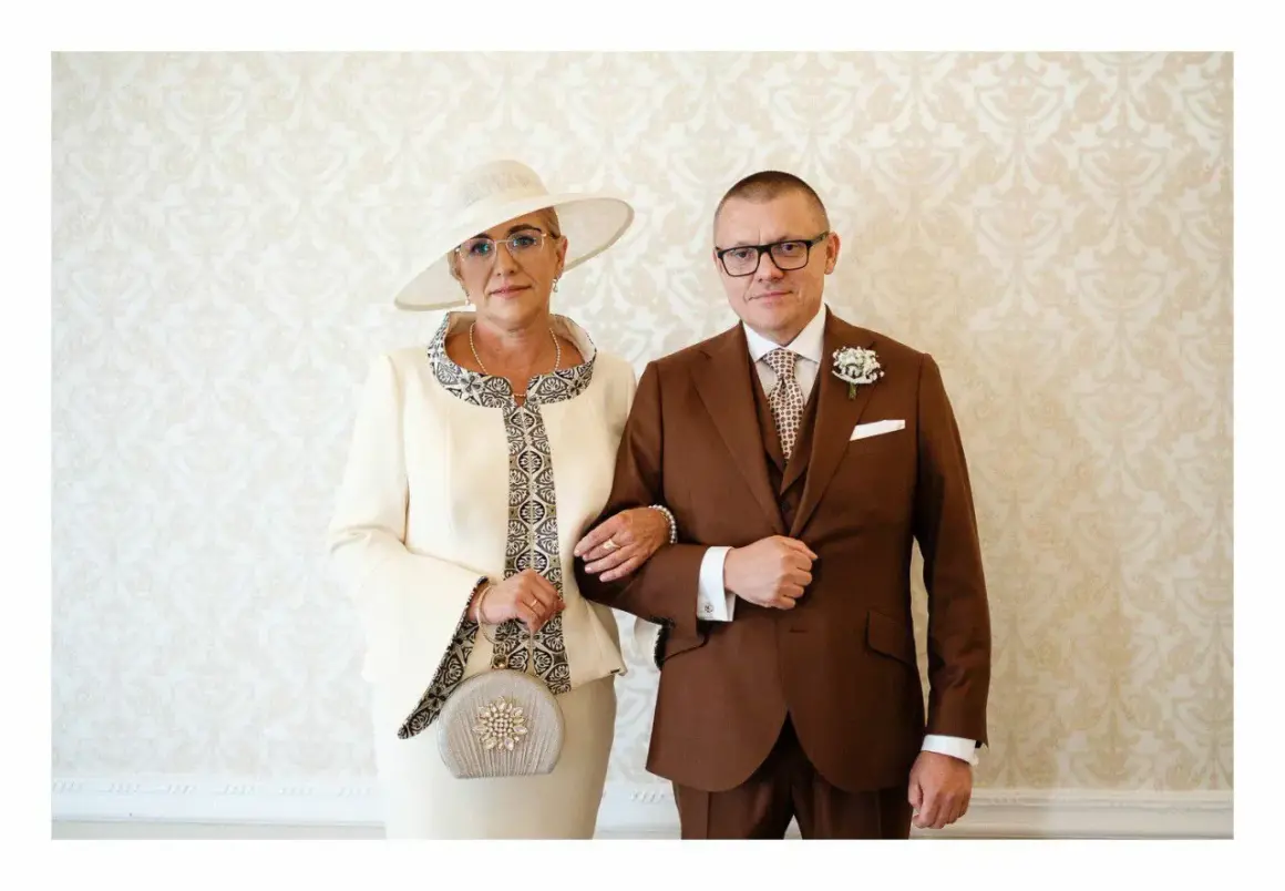 Elegancka mama pana młodego w kremowym kostiumie i kapeluszu, obok syna w brązowym garniturze.
